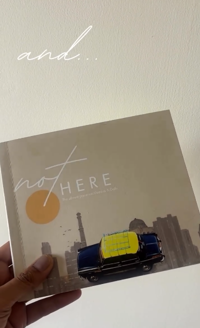 notHERE: The Absent Presence, held in hand, with its taxi-and-skyline cover art