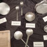 On display at the Museo Camera by Camerawaali, steel utensils flatlay (tiffin carrier, soup spoons, katoris, flower basket)