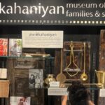 On display at the Museo Camera by Camerawaali, the case with the cheeni cups placard and a visitor crouched at the shelf