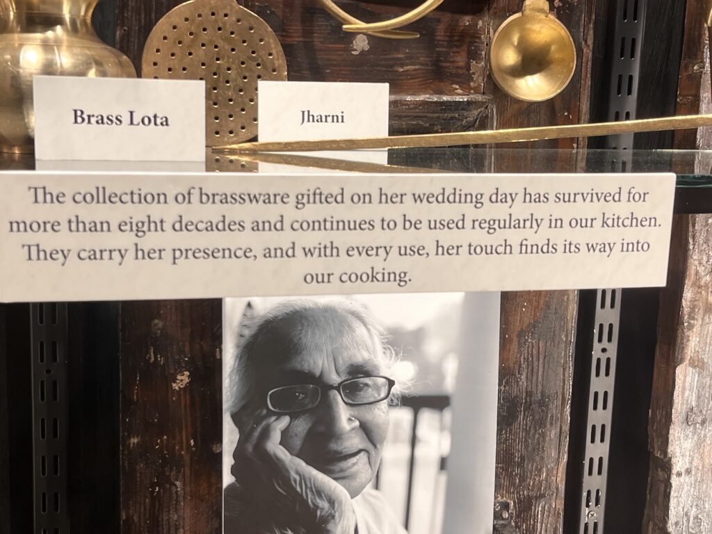 Close-up of Brass Lota and Jharni object labels above wall text about wedding-day brassware, beside a portrait of the grandmother.