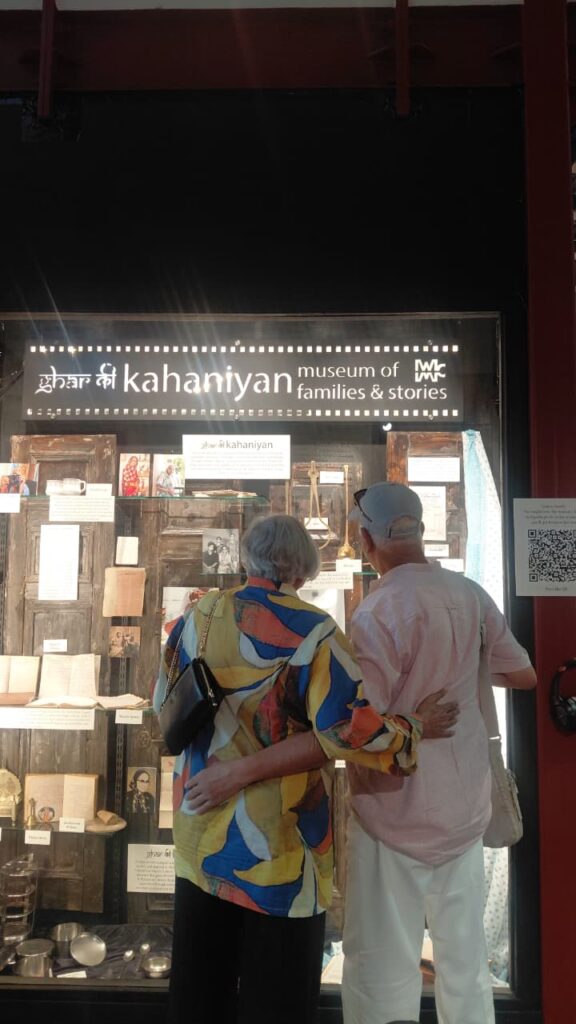An elderly couple standing arm in arm, viewing the "Ghar Ki Kahaniyan" installation together at Museo Camera, Gurugram